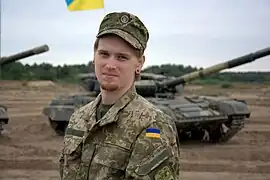 A Ukrainian soldier in standard camouflage dress with tanks in the background