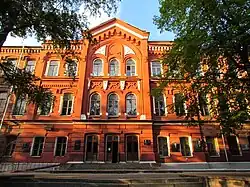 Brown, three-story building with arched windows and trees in front