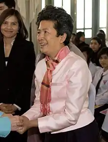 Tuenjai Deetes shaking hands with a woman at an event, smiling, wearing a pink jacket and scarf.