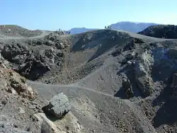 Small figures of people can be seen at the top looking into craters strewn with grey rocks.