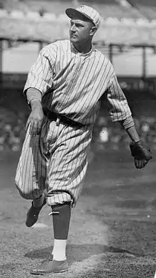 A man in a white baseball uniform with dark pinstripes having just thrown a ball.