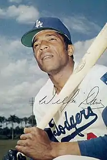 A man in a white baseball jersey and blue undersleeves and cap