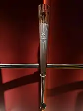 Tall and slender conical torch, composed of metal and glass, with the Olympic Rings logo, and the 2002 Winter Olympics logo