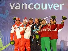 six men stand together wearing Paralympic medals and waving flower bouquets