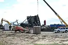 In the distance, a massive crumpled metal oil rig frame is surrounded by debris.