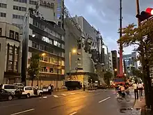 Scaffolding hanging from the side of a building and partially lying on a road, which has been cordoned off.