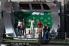 Four men standing on the mounted stands on the podium with officials to their left after the 2019 Hungarian Grand Prix