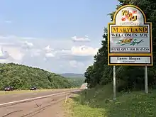 A sign adjacent to a four-lane highway reads "Maryland welcomes you. We’re Open For Business. Larry Hogan, Governor"