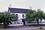 Double storey, now double pile symmetrical three bay plan. Double pitch asymmetrical corrugated iron roof. Walls brick plastered. Mixture of small and large pane-sash windows. Bay windows (C1880) downstairs. Original front door. This property was transferred to Piet Retief on 16 July 1821. It is presumed that he built the oldest portion of this building, although the remaining portion of the double-storeyed house dates from the eighteen-forties. Another prominent pioneer of the E Type of site: House Current use: Domestic – House. This property was transferred to Piet Retief on 16 July 1821. It is presumed that he built the oldest portion of this building, although the remaining portion of the double-storeyed house dates from the eighteen-forties.