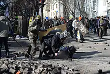 Man on the ground being beaten by two other men, with soldier with club behind them