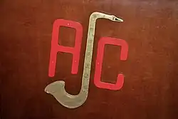 A sculpture resembling the logo of the Antwerp Jazz Club, attached to the front of the foldable wooden screen covering the presenter's area, present during the jazz club's Tuesday-evening sessions in its clubhouse (13 September 2016).