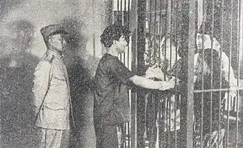 A shot from the film featuring Soebagio talking to people from behind bars, supervised by an officer