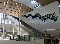 Spacious station interior with white walls and tan ceiling and large windows high up on the walls