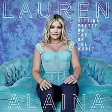 A woman wearing an aqua top and blue jeans, sitting on a teal couch against a violet and blue background. The artist's first and last name appear above and below her, written in white transparent text. The album title is on the right side, stacked and written in white text.