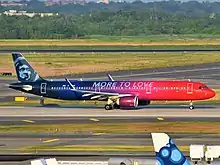 A plane that is painted in red in the front and navy blue in the back, with a red-to-blue ombre in the middle, a navy blue eskimo on the tail, and the words "MORE TO LOVE" across the fuselage, is taxiing on an airport taxiway