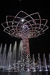 Large tree made of lights at night, surrounded by fountains