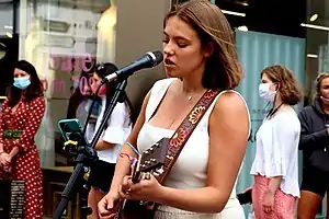 A teenage girl plays guitar by a  microphone on a street