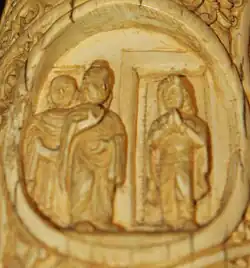 Ivory tusk with three figures: the Buddha, another attending monk, and a female figure standing in a doorway.