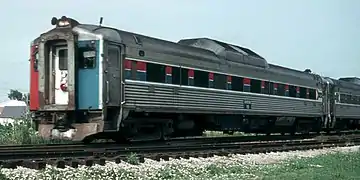 Stainless steel passenger rail cars with red and blue stripes horizontally across the windows. The visible end is covered with three vertical red, white, and blue stripes.