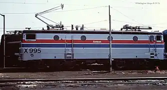 A gray electric locomotive with a black roof and red and blue side stripes