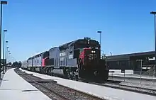 A long passenger train led by diesel locomotives arriving at a railway station