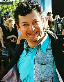 A photograph of Andy Serkis, a dark-haired man wearing a blue shirt and a dark blazer.