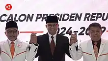 Photo of three person holding their hand upwards. Anies Baswedan (middle) wearing black suit with PKS President Ahmad Syaikhu (left) and Sohibul Iman (right) wearing white suit during PKS endorsement for Anies Baswedan.