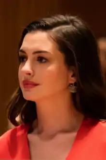 A headshot of Anne Hathaway in an orange outfit