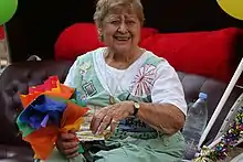 A woman with short brown hair sitting in a carriage, holding a bundle of rainbow cloth or papers