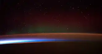 Earth's atmosphere seen from space. From the bottom, afterglow illuminates the troposphere in orange with silhouettes of clouds, and the stratosphere in white and blue. Next the mesosphere (pink) and the pink line of airglow of the lower thermosphere (dark), which hosts green and red aurorae over several hundred kilometers.