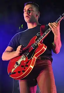 A man wearing a dark gray shirt playing a red electric guitar on stage