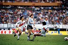 Photograph of four men on a football pitch pursuing a ball during a game