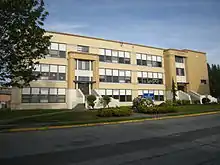 A three-story tan-and-beige building on the side of a road.