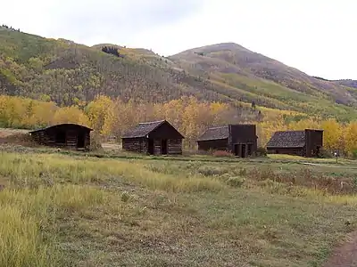 Four small old wooden houses seen at some distance with high hills in the background.