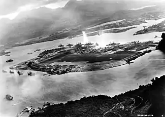 Photograph from a Japanese plane of Battleship Row at the beginning of the surprise Attack on Pearl Harbor. The explosion in the center is a torpedo strike on the USS Oklahoma. Two attacking Japanese planes can be seen: one over the USS Neosho and one over the Naval Yard.