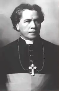 A man wearing a clerical collar and pectoral cross around his neck faces towards the right.