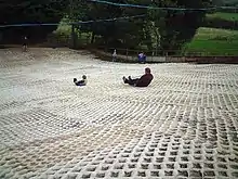 Photograph of the dry ski slope at the Mendip Snowsport Centre with two people tobogganing down the slope