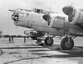 Four-engined bombers with spinning propellers parked on an airfield