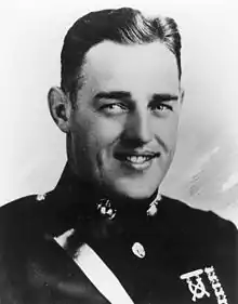 Head of a young white man with neatly combed dark hair in a military jacket with a strap diagonally across the chest and badges pinned to his left breast