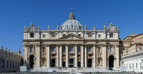 Ornate building in the early morning with a giant order of columns beneath a Latin inscription, fourteen statues on the roofline, and large dome on top.