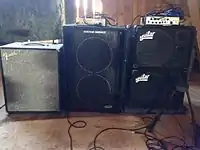 A Fender bass cabinet, a Genz Benz bass cabinet, and two Aguilar cabinets are shown. The Genz Benz and Aguilar cabinets each have amplifier "heads" sitting on top.