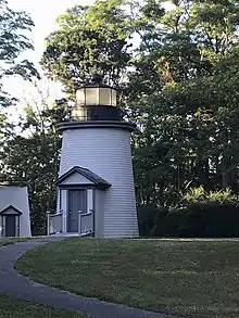 Photo showing the Beacon Lighthouse which has the main light on top. The lighthouse is mainly white with a large grey door.