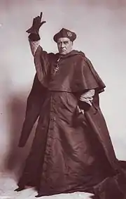  Middle=-aged, clean-shaven white man in the robes of a 16th-century cardinal