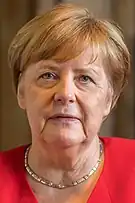 Formal portrait of Angela Merkel looking neutral in a red jacket with gold simple neckless