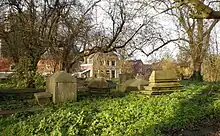 A view of the Jewish cemetery, Beth Haim, showing a various tombs among trees, with buildings in the background.