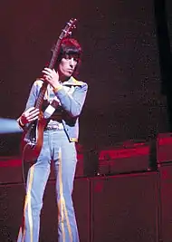 Bill Wyman holds a bass guitar onstage.