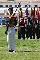 Photo of uniformed man holding a 19th century musket. He wears a replica blue coat and shako from the early 1800s.