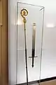 High Court Executioner's sword with Christian epigram, ca. 1760 Salzburg, Austria, on display next to a Bishop's staff. The executioner's sword is designed as a cutting weapon rather than stabbing, forged of brass and iron.