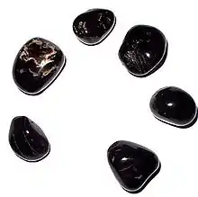 "A photograph of 6 smooth black pebbles with white markings which are arranged in a circle"