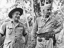 Two men in uniforms, without ties. One wears a garrison cap while the other wears a slouch hat.